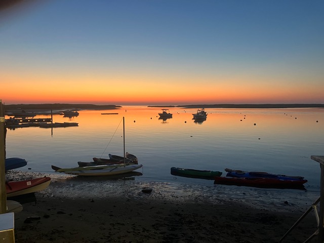 Sunset over Pamet Harbor with kayaks pulled up on the sand