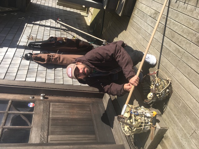 A clammer with a rake and two baskets of harvested clams