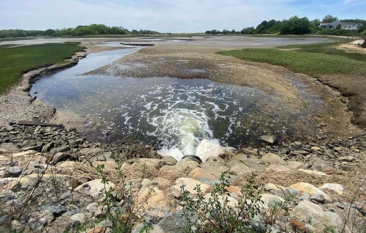 Water pouring through the 36-inch pipe beneath Mill Pond Road between rock-armored banks